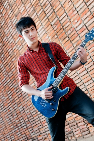 Handsome young musician playing the guitar and singing at the red wall.の写真素材