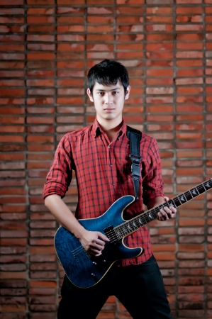 Handsome young musician playing the guitar and singing at the red wall.の写真素材