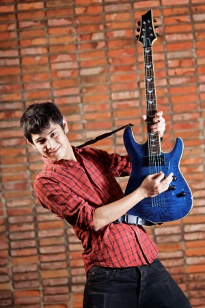Handsome young musician playing the guitar and singing at the red wall.の写真素材