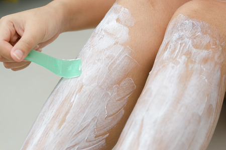 Body hygiene: Woman depilates - scrubs hair removal cream off her leg 