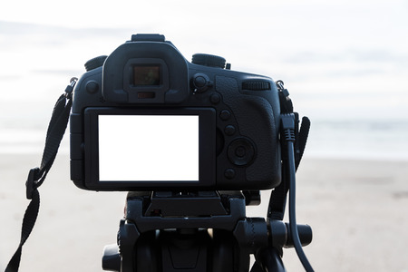 Digital camera on the tripod isolated white screen at the beach background