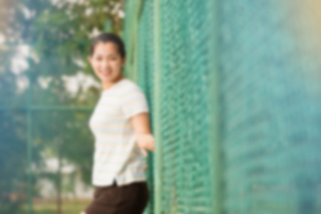 Blur effect of asian female relax and smile standing on tennis court and looking at camera