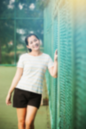 Blur effect of asian female relax and smile standing on tennis court and looking at cameraの写真素材