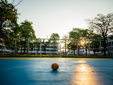 Old yellow soccer ball on the blue football field on the day of sunrise.の写真素材