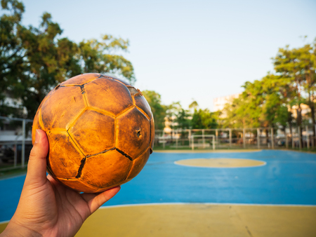 A man holding a yellow soccer ball on a blue football field on a bright day.