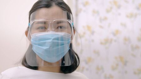 Portrait of an Asia young female who is wearing a face shield with mask rounded around her face from a frontal perspective to protect her glasses and eyes prepare to new normal. Coronavirus pandemic.の写真素材
