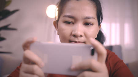 Asian women on redshirt using a smartphone for gaming online with excited emotion in living room