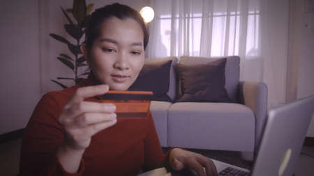 Asian women on redshirt using the laptop and credit card for shopping online in pandemic situation...