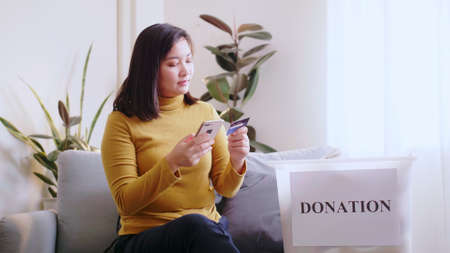 Asian woman pressing phone using a credit card to pay online to reserve donation box delivery.