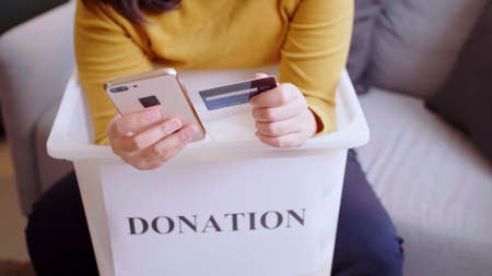 Asian woman pressing phone using a credit card to pay online to reserve donation box delivery.の写真素材