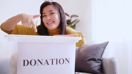Asian woman pointing to a donation box inviting people to join the campaign to donate unused items.の写真素材