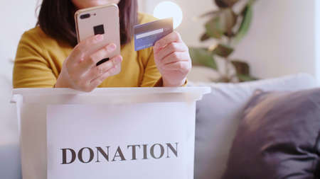 Asian woman pressing phone using a credit card to pay online to reserve donation box delivery.の写真素材