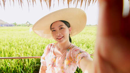 Woman in hat on video call showing rice field with happy day in summer.の写真素材