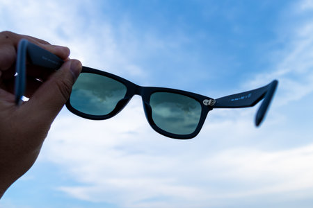 A person showcases stylish sunglasses against a bright blue sky.