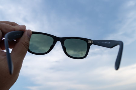 A close-up of sunglasses held against a beautiful sky showcasing style and outdoor vibes.の写真素材