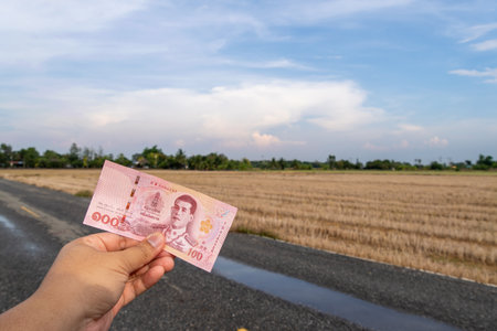 A person holds a banknote against a scenic rural backdrop symbolizing economic value.