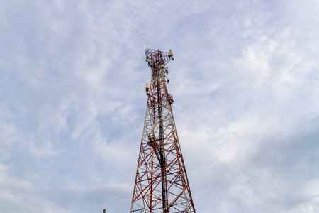 A telecommunication tower stands tall against a cloudy sky showcasing urban infrastructure and...