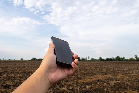 A farmer uses a smartphone to monitor crop conditions in a vast rural landscape.の写真素材