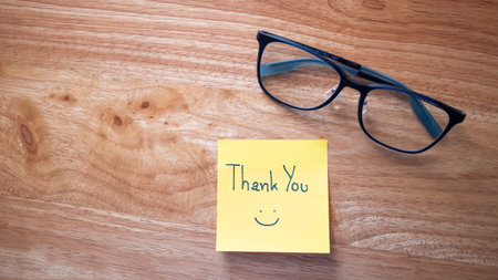 A heartfelt thank you note placed beside glasses symbolizes appreciation in a cozy workspace.の写真素材