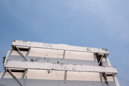 An abandoned building facade contrasts against the clear blue sky showcasing urban decay and...