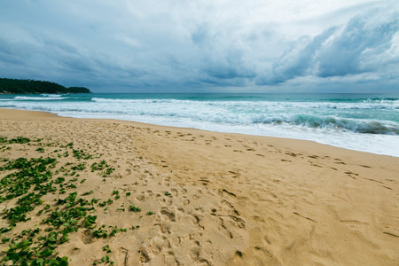 A peaceful beach scene where waves crash onto the shore under a dramatic moody sky.の写真素材