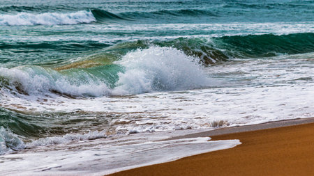 Experience the serene beauty of ocean waves gently crashing a sandy beach at dawn.の写真素材
