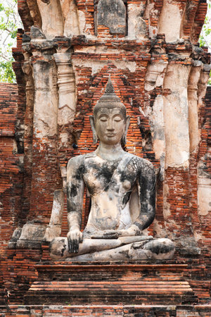 Explore the serene presence of an ancient Buddha statue amidst historic ruins reflecting Thailand's rich cultural heritage.の写真素材