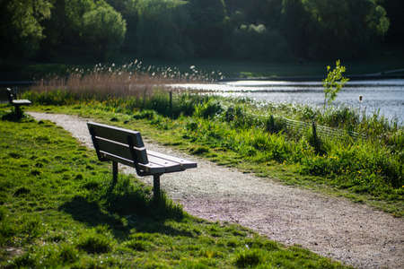 A bench by a lake on a beautiful sunny Spring day with sunlight reflections on the water.の写真素材