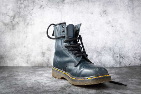 A used black leather boot isolated with a concrete background
