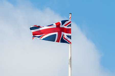 The national flag of the United Kingdom also known as the Union Jack flying in the wind with a blue sky cloud background.の写真素材