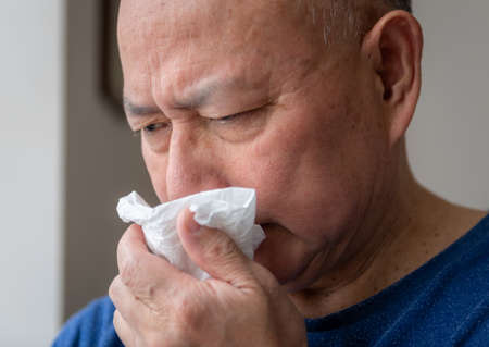Closeup of a matured man sneezing into a paper tissue.の写真素材