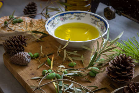 Green olives and branch on a wooden board with a bowl and a bottle of home cold pressed olive oil.の写真素材