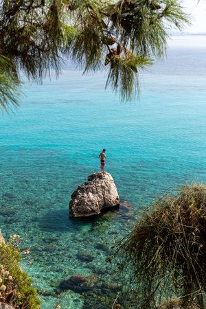 Lefkada island. Greece- 08.05.2021: a tourist standing on a rock ready to dive into the beautiful turquoise sea.のeditorial素材