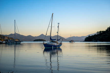 Sailing yachts in calm waters casting reflections in morning light.の写真素材