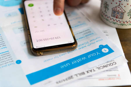 A person using a phone calculator to work out cost of utility and tax bills. Inflation, cost of...