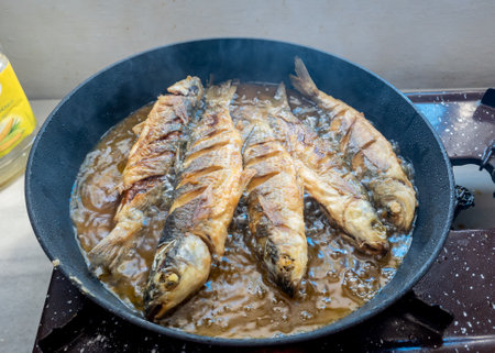 Freshly caught grey mullets frying in a pan with olive oil.