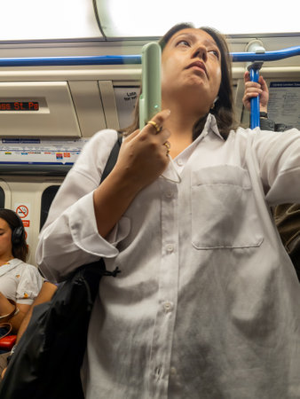 London. UK- 08.16.2023. A female passenger on the London Underground using a hand held electric fan...