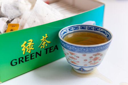 A cup of green tea by a box of tea tea bags isolated in white. Healthy drink, lifestyle concept.の写真素材