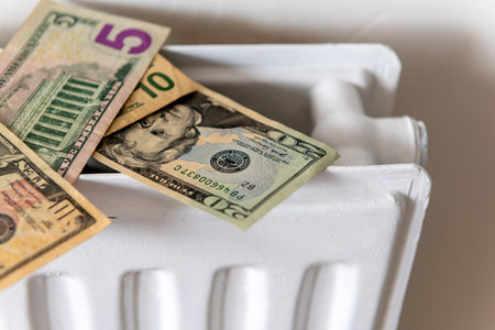 A bunch of US Dollars on top of a central heating radiator. A heating, energy cost concept.の写真素材