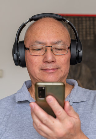 A senior man relaxing at home listening to online music with wireless headphone and a smartphone. A technology use concept.の写真素材