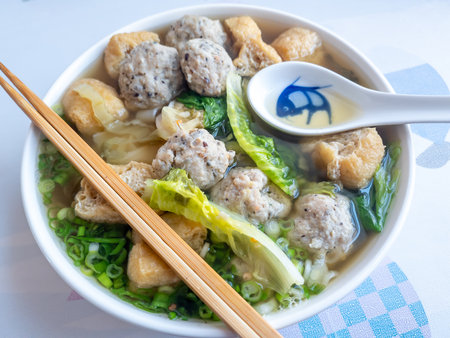 A delicious bowl of meat ball and fried tofu ho fun soup with lettuce and spring onions.の写真素材
