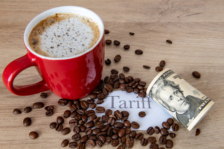 A cup of coffee, coffee beans, the printed word tariff and a roll of US Dollar bills on a table. A coffee tariff concept.の写真素材