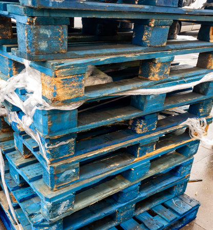 A stack of well used heavy duty wooden pallet on the street outside a grocery supermarket.