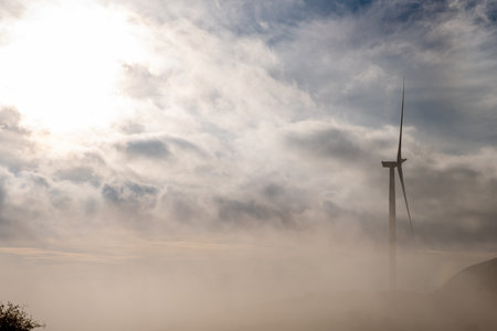 A wind turbine on a mountain top wind farm at dawn partially covered in mist.の写真素材