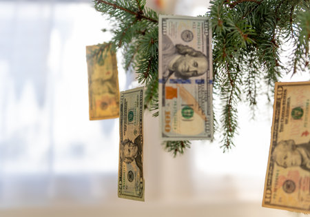 Various US Dollar bills hanging on a Christmas tree as ornaments with a bright, light background. A Christmas cost concept.の写真素材