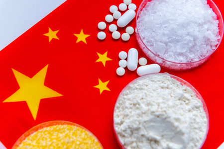A close up top view of medicine base substances in glass trays and loose medicine tablets on the national flag of China. A Chinese pharmaceuticals concept.の写真素材
