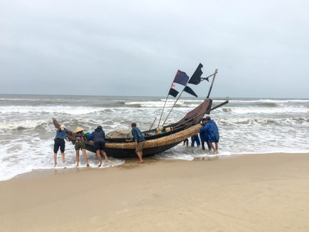 Quang Tri, Vietnam - February 11, 2020: People push a fishing boat out to sea during a windy day at the beach of Quang Tri province, Vietnamのeditorial素材