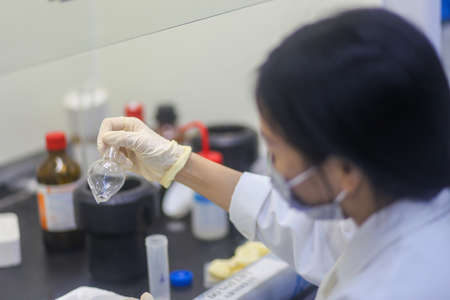 Closeup of an Asian woman scientist checking glass flask of an experiment in the laboratory