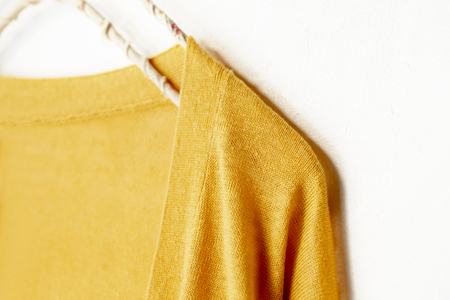 a cardigan in yellow hanging on clothes hanger on white background.Close up.