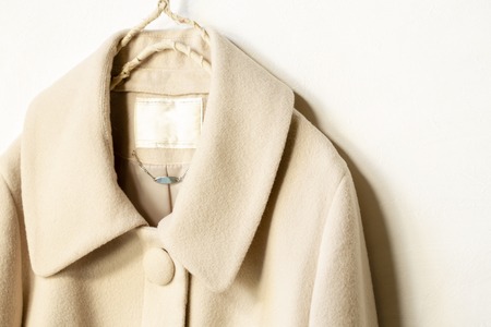 beige wool coat hanging on clothes hanger on white background.close up.の写真素材